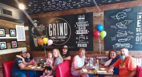 A family sits at a restaurant booth, smiling with balloons, in front of a wall featuring fun food-themed artwork.
