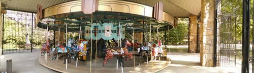 A vintage carousel with colorful horses, set in a park under a covered pavilion.