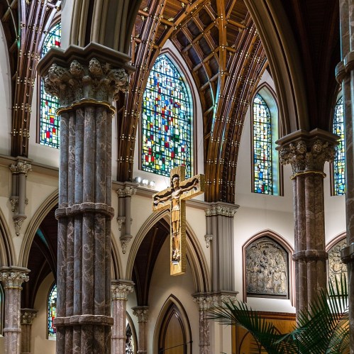 Interior of a church featuring stained glass windows, ornate columns, and a large crucifix hanging from the ceiling.