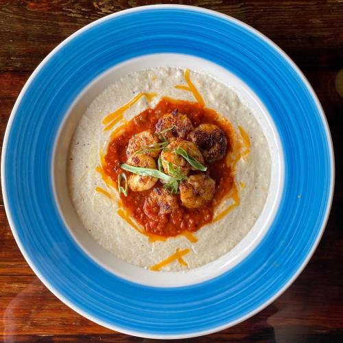 A blue-rimmed plate with creamy grits topped with shrimp in a spicy tomato sauce and garnished with green onions.