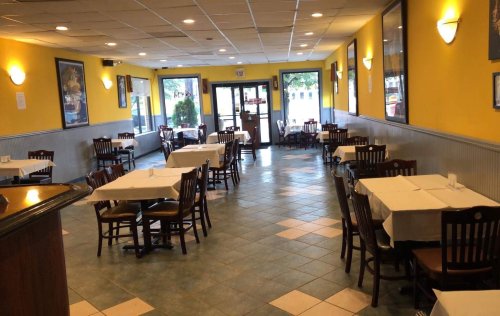 Interior of a restaurant with yellow walls, empty tables covered in white tablecloths, and large windows letting in light.