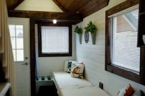 Cozy interior of a tiny home with a bench, decorative plants, and large windows letting in natural light.