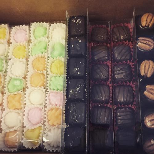 A variety of colorful chocolates and confections arranged in clear boxes, showcasing different shapes and textures.