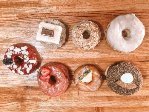 A variety of colorful donuts arranged on a wooden surface, featuring toppings like fruit, nuts, and chocolate.