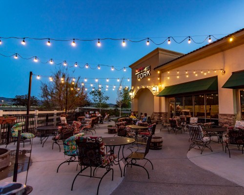 Outdoor dining area of a restaurant with string lights, colorful chairs, and a cozy atmosphere at dusk.