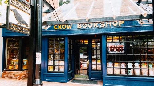 Exterior of Crow Bookshop featuring a blue facade, large windows, and a sign for new and used books.