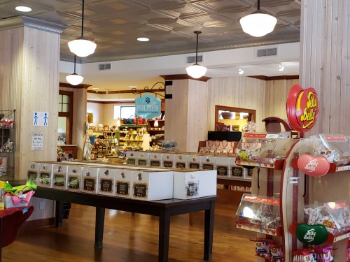 Interior of a charming store with wooden decor, shelves filled with candy, and a display of jars on a table.
