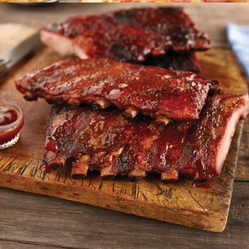 Deliciously glazed barbecue ribs on a wooden cutting board, with a side of sauce.