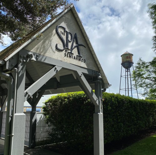 Sign for "The Spa Semiahmoo" with a water tower in the background, surrounded by greenery.