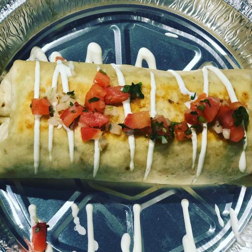 A large burrito topped with diced tomatoes and drizzled with sour cream on a silver plate.
