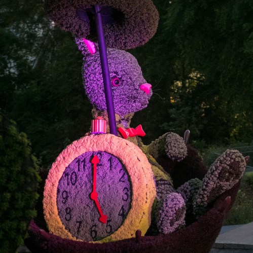 A whimsical topiary of a rabbit holding a clock, illuminated with colorful lights in a garden setting.