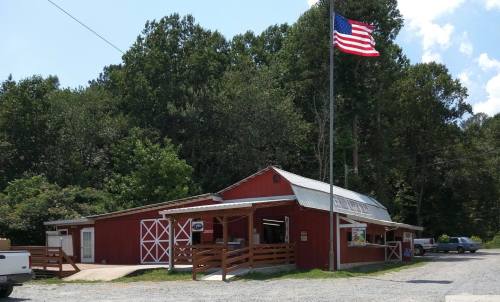 A red barn-style building with a flagpole, surrounded by trees and gravel, featuring a small outdoor service area.