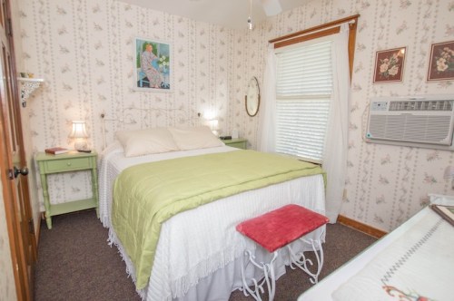 Cozy bedroom with a double bed, floral wallpaper, green accents, and an air conditioner by the window.