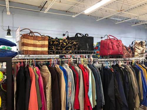 A clothing rack filled with various jackets and coats, with bags displayed on a shelf above.