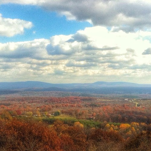 A scenic view of rolling hills and vibrant autumn foliage under a partly cloudy sky.