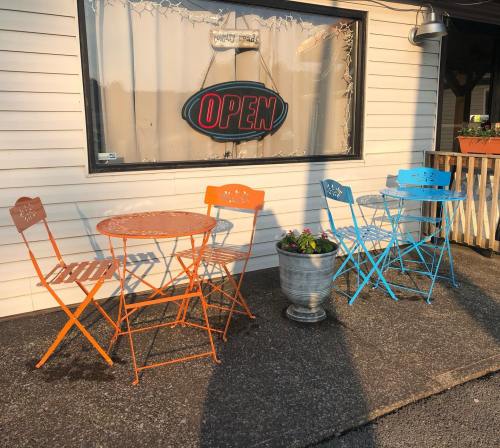 A cozy outdoor seating area with orange and blue metal tables and chairs, next to a flower pot, in front of an "OPEN" sign.