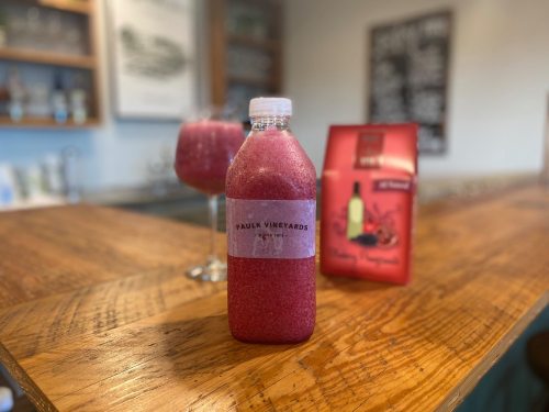 A bottle of pink beverage labeled "Paul Vineyards" on a wooden bar, with two glasses and a menu in the background.