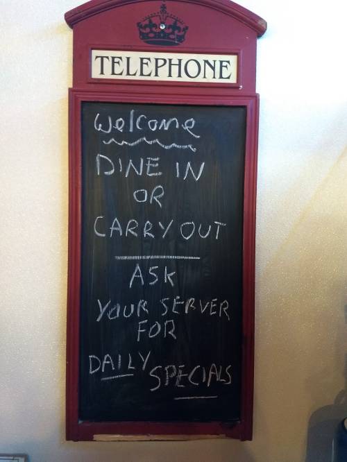 A chalkboard sign welcoming customers for dine-in or carryout, with a note to ask servers about daily specials.