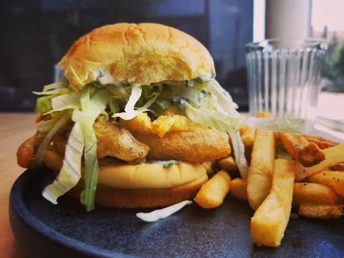 A crispy fried fish sandwich topped with lettuce, served with a side of golden French fries on a blue plate.