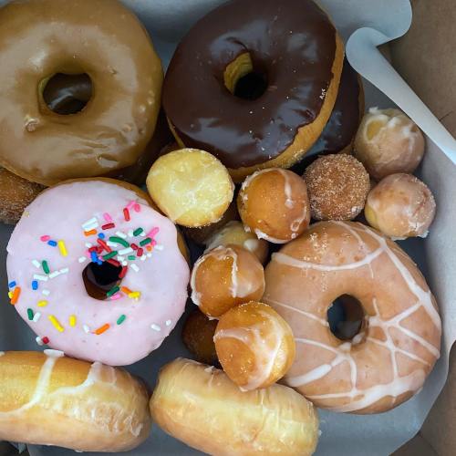 A variety of donuts in a box, including glazed, chocolate, and sprinkled options, along with mini donuts.
