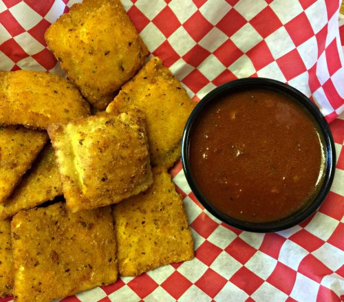 A basket of golden-brown, crispy squares with a side of red dipping sauce on a checkered paper background.