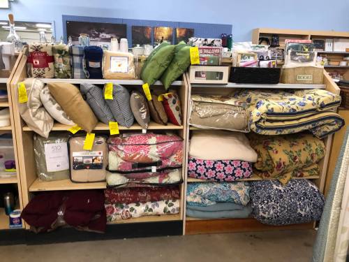 Shelves displaying various bedding items, including quilts, comforters, and decorative pillows, with price tags attached.