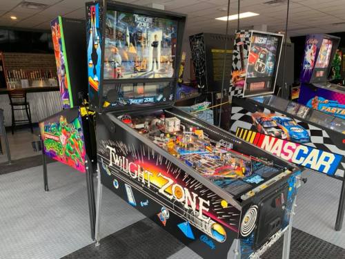 A colorful pinball machine themed after "Twilight Zone" in an arcade, surrounded by other game machines.