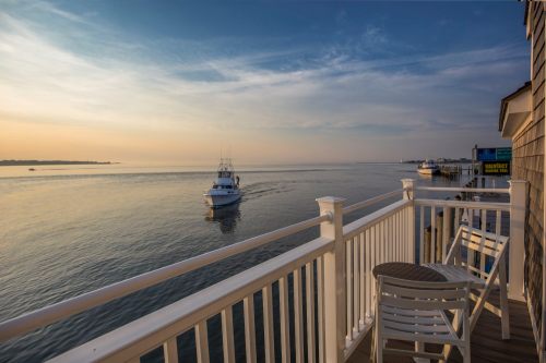 A serene waterfront view from a balcony, featuring a boat on calm waters and a soft sunrise in the background.