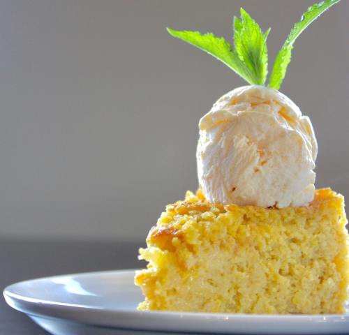 A slice of cake topped with a scoop of ice cream and a mint leaf, served on a white plate.