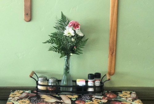 A vase with flowers sits on a table, accompanied by a spice rack and a colorful tablecloth.