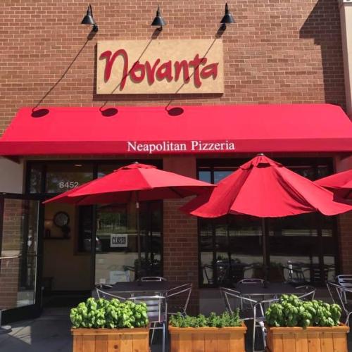 Exterior of Novanta Neapolitan Pizzeria featuring a red awning, outdoor seating, and potted plants.