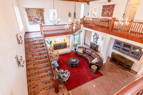 Spacious living room with a red rug, leather sofa, and elegant chandeliers, viewed from an upper level.