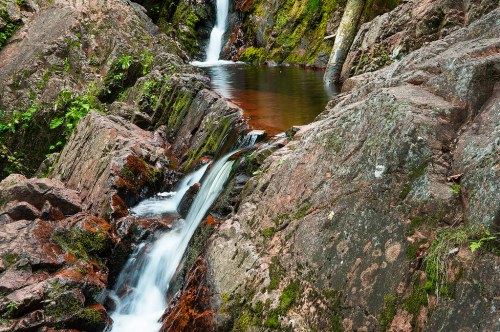 A serene waterfall cascading over rocky terrain, surrounded by lush greenery and a calm pool of water below.