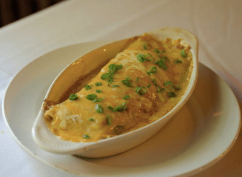 A baked dish of enchiladas topped with melted cheese and green onions, served in a white oval dish.