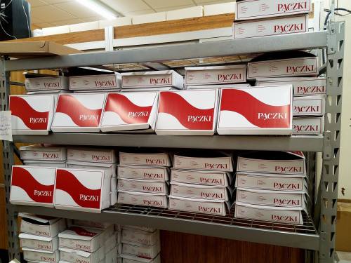 A shelf filled with neatly stacked boxes of paczki, a traditional Polish pastry, in a bakery setting.