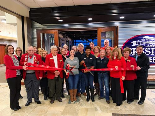 A group of people in red jackets and business attire gather for a ribbon-cutting ceremony at a new venue.