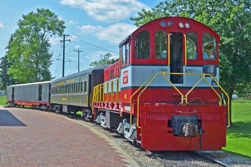 A red and yellow diesel locomotive with a passenger car parked on a track surrounded by greenery and blue skies.
