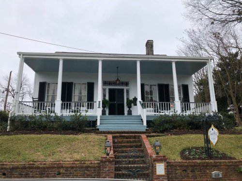 A charming blue house with a large porch, white columns, and green shutters, surrounded by a well-kept lawn.