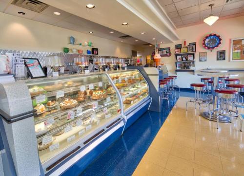 A retro-style dessert shop featuring a glass display case filled with pastries and a seating area with red stools.