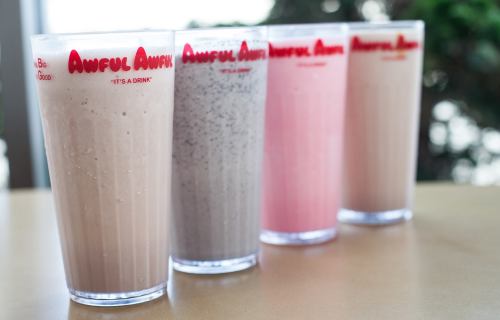 Four tall glasses of milkshakes in various colors: chocolate, gray, pink, and a lighter shade, all labeled "Awful Awful."