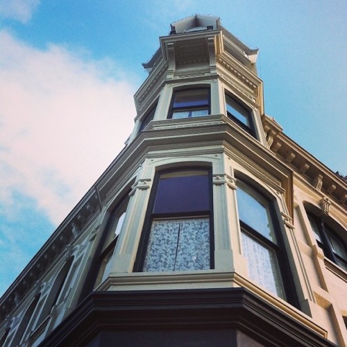 A tall, ornate building with large windows, viewed from below against a blue sky with scattered clouds.