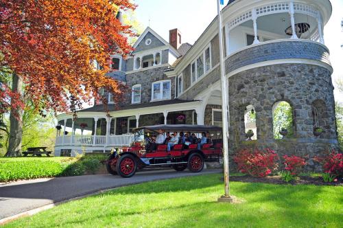 A vintage car parked in front of a large stone mansion surrounded by colorful trees and blooming flowers.