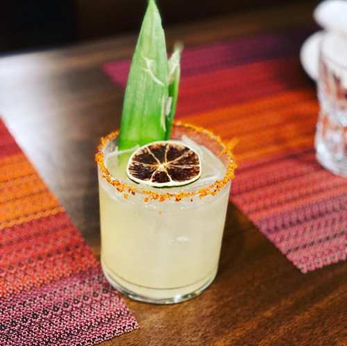 A refreshing cocktail in a glass, garnished with a dried lime slice and a green leaf, on a colorful table setting.
