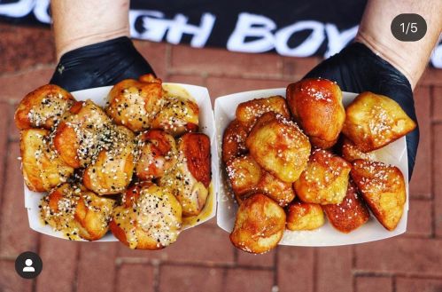 Two hands holding two trays of golden, glazed dough balls, one topped with sesame seeds and the other with a shiny glaze.