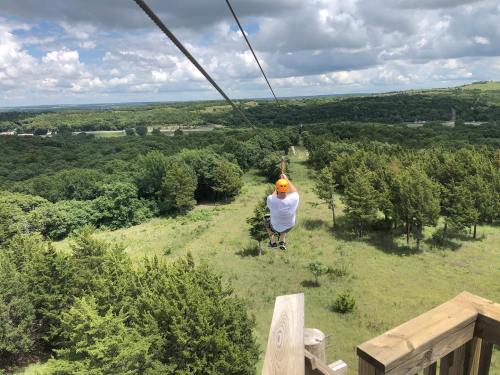 A person zip-lining over a green landscape with trees and a cloudy sky in the background.