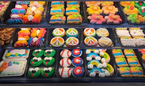 A colorful display of decorated cookies and pastries in various shapes, including flowers, peace signs, and rainbows.