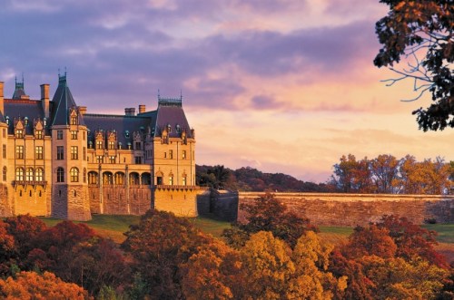 A grand castle surrounded by colorful autumn trees under a vibrant sunset sky.