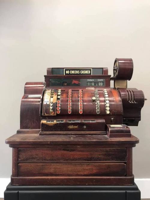 A vintage wooden cash register with a sign reading "No Checks Cashed" on top.