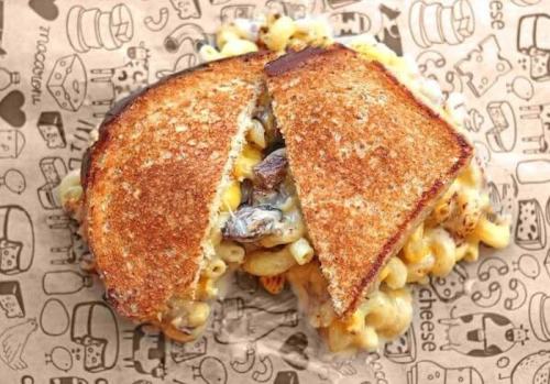 A grilled cheese sandwich filled with macaroni and cheese, cut in half, on a patterned paper background.