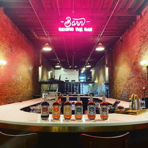 A bar with a neon sign reading "Bar" and various bottles of spirits lined up on a white countertop.